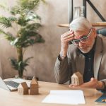 We Buy Houses Ripoffs: 8 Red Flags & How To Avoid Them A stressed male homeowner who falls for a We Buy Houses ripoff sits at his desk.