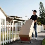 How To Clear Out Your House And Sell Your Home Fast Man moving boxes on dolly outside suburban house.