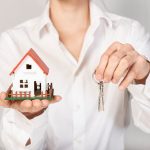 A woman holding a miniature house and key house