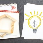 Home value improvement concept with wooden house model and lightbulb containing dollar sign.