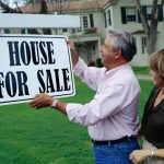 Couple holding sign for selling house