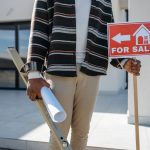 A man holding a “House for Sale” sign
