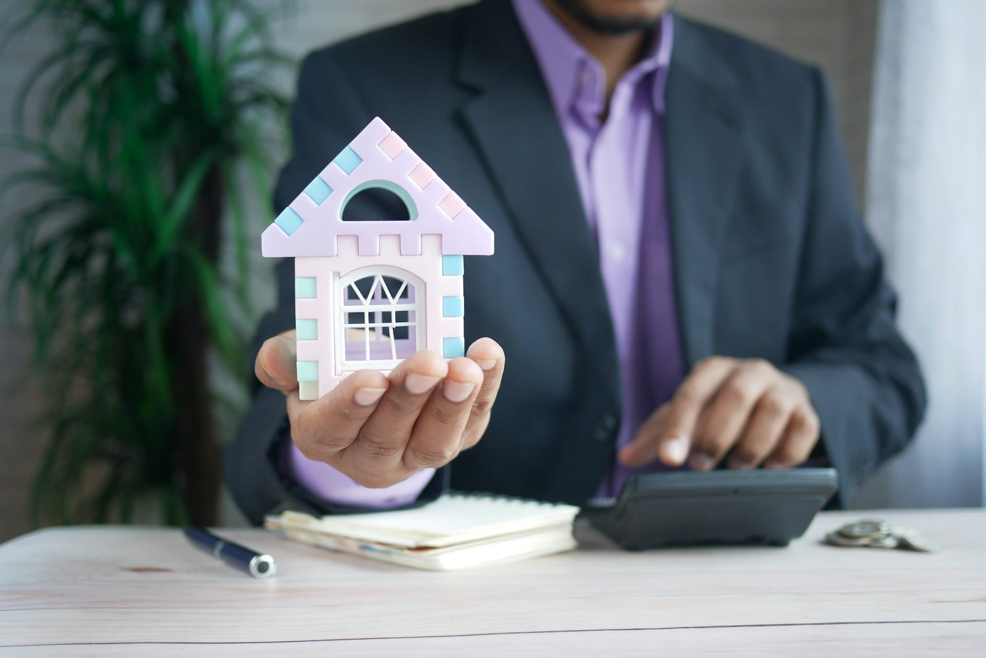 A man holding a miniature house while calculating