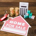 5 Home Improvements With The Best ROI Calculator and coins beside home sale sign for ROI planning purposes.