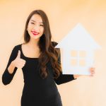 The 20 Tips For Increasing Your Home's Value Happy homeowner holding house cutout representing tips for increasing your home's value today.