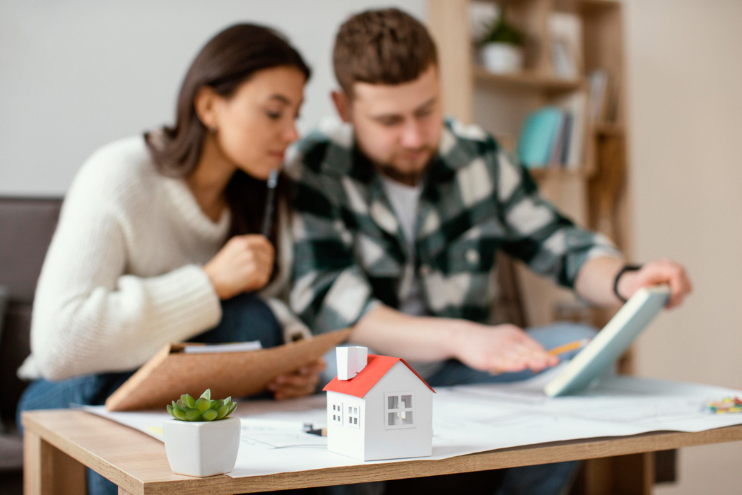 Young homebuyers analyzing Boston home price insights with miniature house on table together.